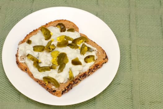 Tamed jalapeno pieces on top of blue cheese and gorgonzola spread on one sprouted grain sesame bread slice.