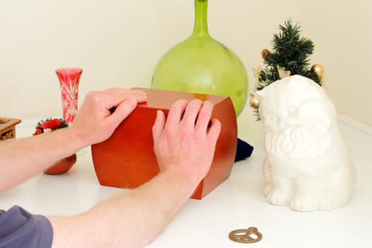 Male caucasian hands holding a wood urn that is on a white mantle surrounded by the departed loved ones mementoes.