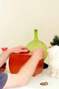 Adult male hands and arms holding onto a wood urn of dear departed ashes surrounded by mementoes on a white fireplace mantle.