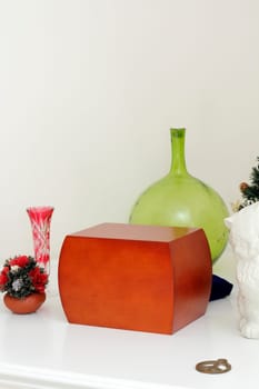 Wood urn filled with loved ones ashes surrounded by memento objects on a white mantle.