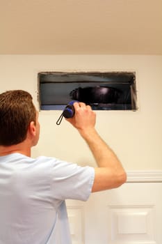 Adult male shining a flashlight into an air duct return vent to check for any need of cleaning dust or any other maintenance.