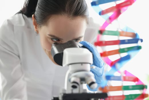 Woman scientist looking through microscope near dna molecule mockup in lab. Scientific genetic research concept