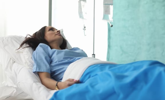 Closeup of young woman laying in hospital bed and waiting for analysis. Clinic patient. Treatment with drop bottle. Medicine and health diagnostic concept