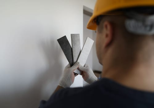 Man in helmet looks at color samples in front wall. Selection colors for wall decoration in apartment. Combination putty in warm and cold colors. Quality work and selected design