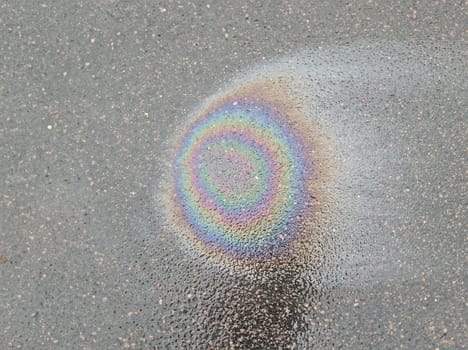 Rainbow stain on wet asphalt from machine oil closeup background. Environmental protection concept