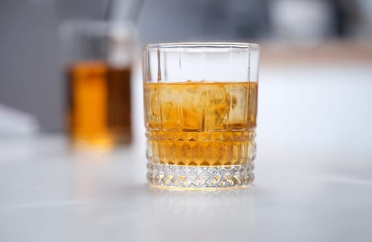 Glass of whiskey with ice standing on table closeup. Alcohol addiction treatment concept
