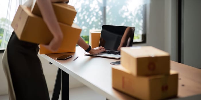 Close up Asian woman using laptop and box to receive and review order online to prepare to pack sell to customers, online small business ideas startup entrepreneur of freelance.