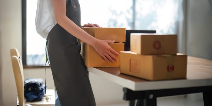 Close up Asian woman using laptop and box to receive and review order online to prepare to pack sell to customers, online sme business ideas startup SME small business entrepreneur of freelance.