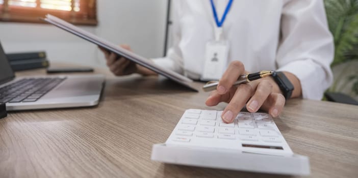 Close up Business woman using calculator and laptop for do math finance on wooden desk in office and business working background, tax, accounting, statistics and analytic research concept.