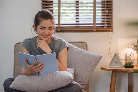 Happy young woman reading book on sofa at home. Lifestyle freelance relax in living room. Lifestyle Concept.