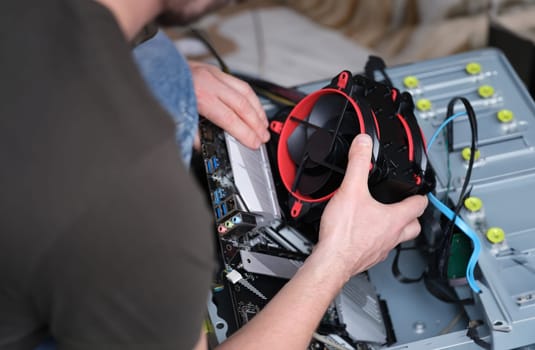 Master repairer holding cooler in front of system unit closeup. Assembly and repair of computer equipment and electronics concept