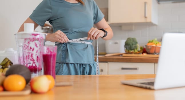 Happy young woman asian measuring waist with smoothie at kitchen.