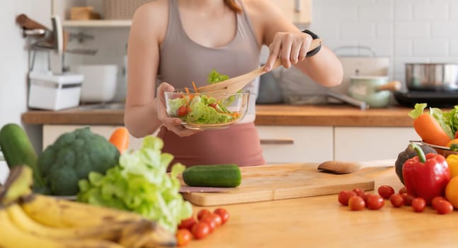 Young woman standing in the kitchen making a salad for health.