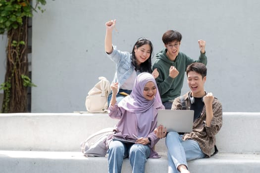 Multiracial smiling group of teenage student using laptop doing homework and enjoying a relaxed atmosphere outdoors at the university campus. Education concept. High quality photo.