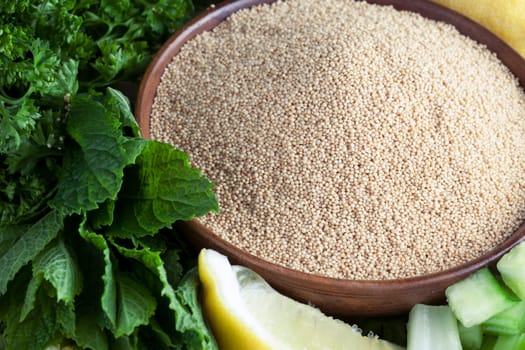 Bowl of amaranth seeds surrounded by mint, parsley and a lemon wedge.