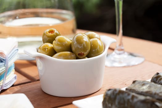 Green olives stuffed with red pimento in small white bowl.