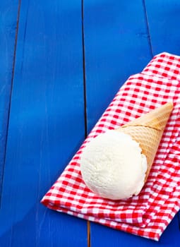 Vanilla icecream served in a cone on a colourful red and white checkered napkin on rustic wooden boards with copyspace