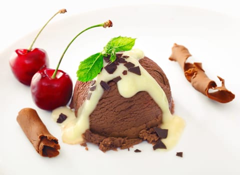 Delicious rich chocolate icecream dessert drizzled with sauce and served with ripe red cherries and coiled shavings of milk chocolate
