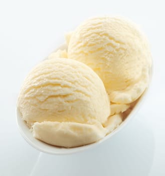 High angle view of scoops of creamy vanilla icecream served in a small white dish on a white background