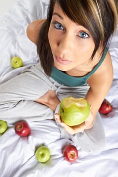 Young woman in bed eating apple