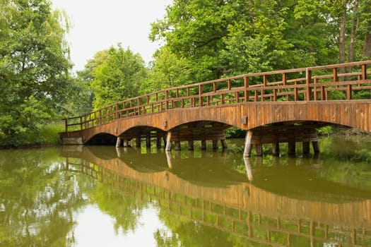 Wooden bridge over a quiet river, lined with green trees (Lednice, Czech Republic)