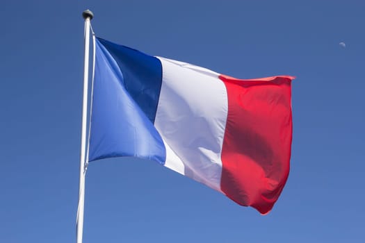 French flag on the mast. Blue sky with the moon in the background.