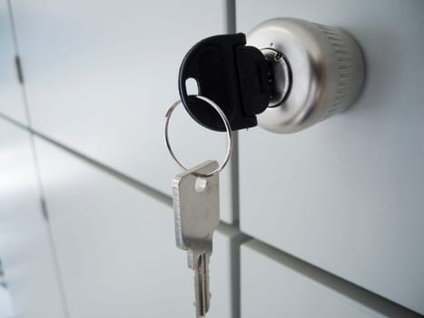 Close-up of a gray cabinet door with a round handle and inserted and hanging keys,as well as intersecting spacer gaps in oblique view