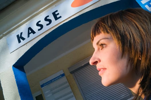 Head and shoulders shot of a young brunette woman in a lower view and a checkout sign in the background
