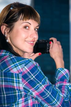 Exterior shot of young brunette woman wearing sunglasses and camera in side view and looking at camera