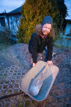 Wide-angle shot of an elderly man bent over with a shovel and a shovel lying in it at dusk and looking into the camera