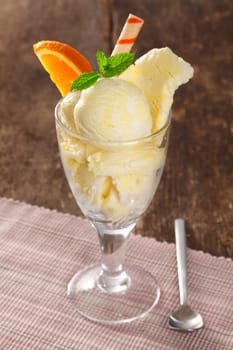 Cold creamy vanilla icecream in a tall glass garnished with mint and orange and a spiral wafer