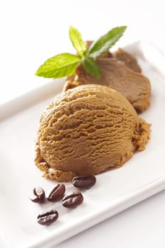 Tilted angle view of a double scoop serving of creamy coffee icecream garnished with mint and coffee beans