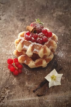 Waffles topped with ripe raspberries dusted with sugar on a rustic wooden table with vanilla pods and redcurrants
