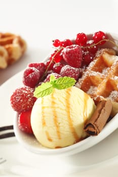 Tilted perspective of a serving of a crisp golden waffle with an assortment of fresh red berries and ice-cream