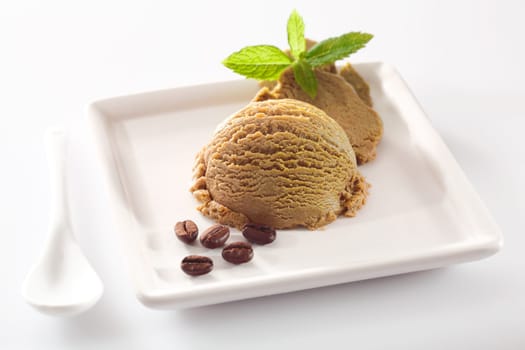 Serving of creamy aromatic coffee ice-cream on a square white porcelain plate with coffee bean garnish
