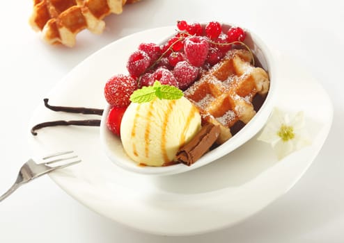 Fresh golden waffle served with icecream and an assortment of red berries including raspberries, redcurrants and strawberries