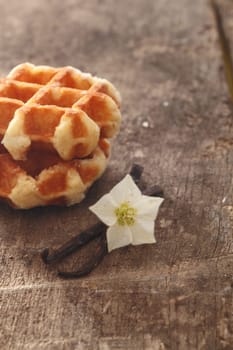 Dried vanilla pods and flower used as flavouring in cooking and baking on a wooden surface with golden waffles