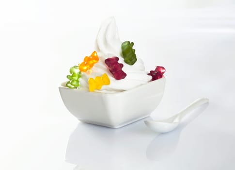 Vanilla softserve icecream in a bowl topped with colourful gummy bears on a white background