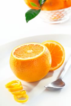 Fresh juicy orange with the top cut off to display the succulent pulp served with a spoon and colied zest