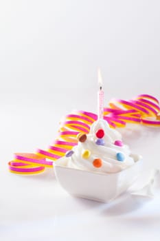 Party ice-cream dessert in a square dish with a single burning birthday candle and spirally coiled decorative ribbon with copy space