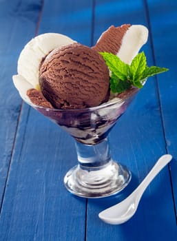 Choclate and vanilla icecream served in a conical glass parfait dish on painted blue wooden boards