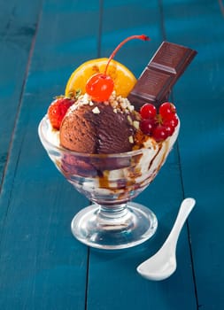 Colourful tropical chocolate dessert with icecream and chocolate squares drizzled with melted chocoalte served with a fresh assortment of tropical fruit on a blue background