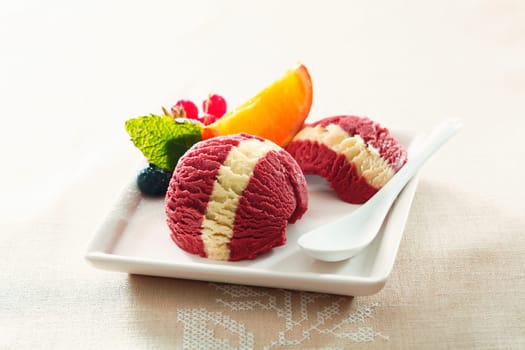 Serving of tropical berry ice-cream dessert with a colourful white stripe and fresh orange and redcurrant garnish