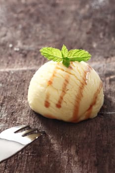 Single scoop of vanilla icecream drizzled with sauce on a textured old wooden table