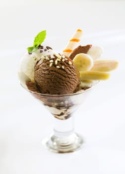 Fresh banana slices served with chocolate and vanilla icecream topped with nuts in a cocktail glass