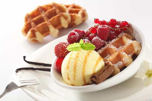 Tilted angle view of a healthy berry and icecream dessert with raspberries, strawberries and redcurrants on a crisp baked waffle