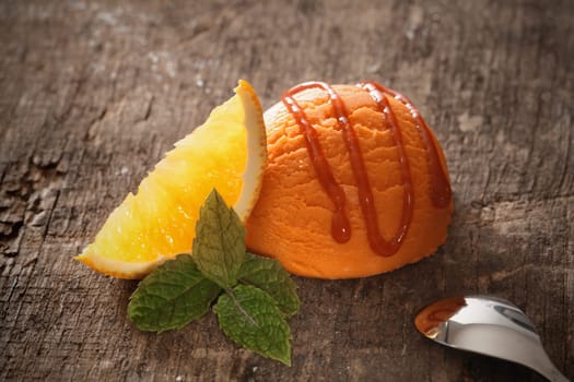 Orange scoop of icecream dessert on a vintage old wooden background, with caramel topping and a fresh slice of orange