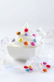 Bowl of twirled softserve icecream topped with colourful round candy chilled by blocks of ice
