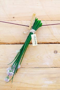 Bunch of fresh green chives with a decorative label hanging from a clothes peg against a rustic wooden background