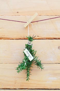 Fresh rosemary herb with a name label hanging from a clothespeg against wooden planks